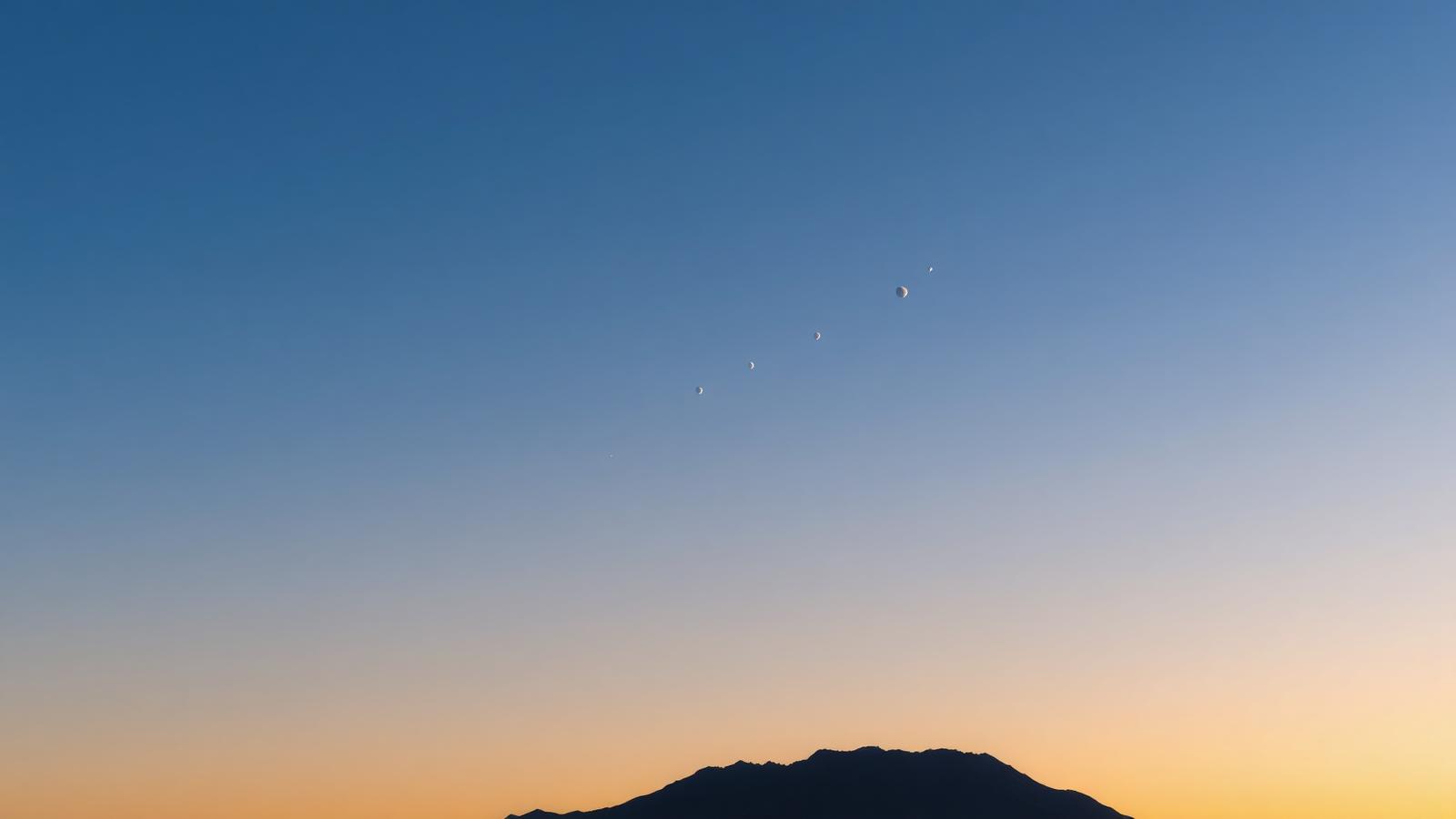 Wide sunset sky with the Moon, Venus and Jupiter aligned along the ecliptic above a mountain silhouette