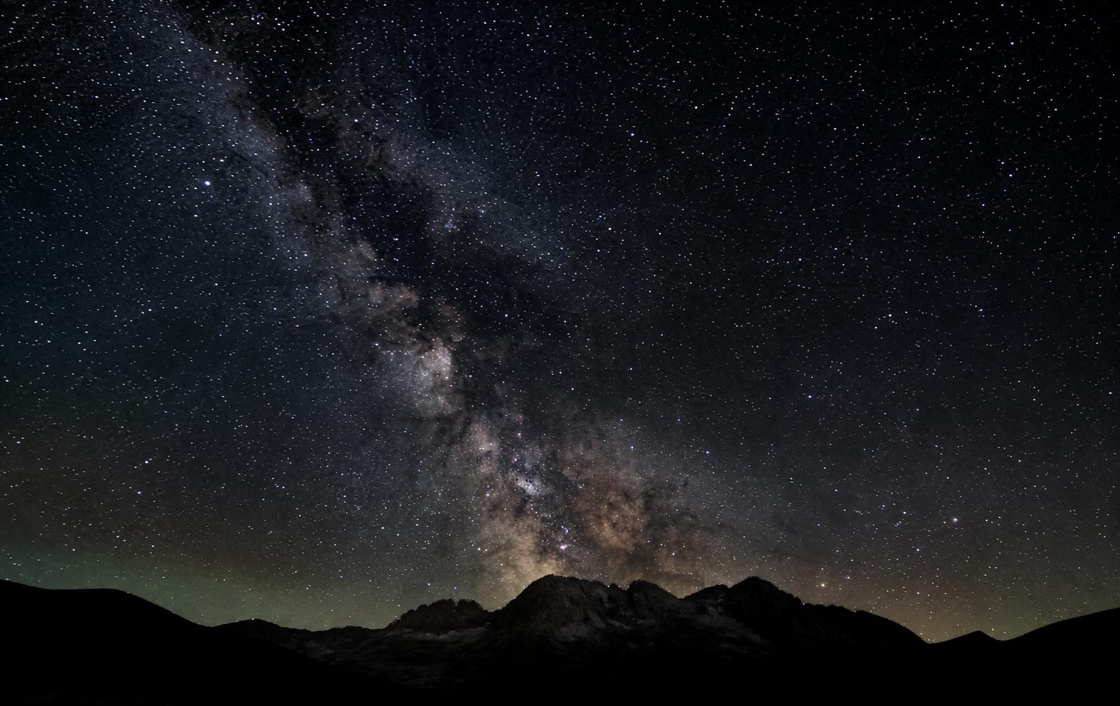 A dark, star-filled sky with the Milky Way rising above a mountain silhouette