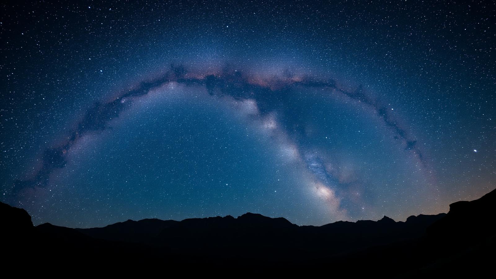 The Milky Way galactic core arching over a dark mountain horizon