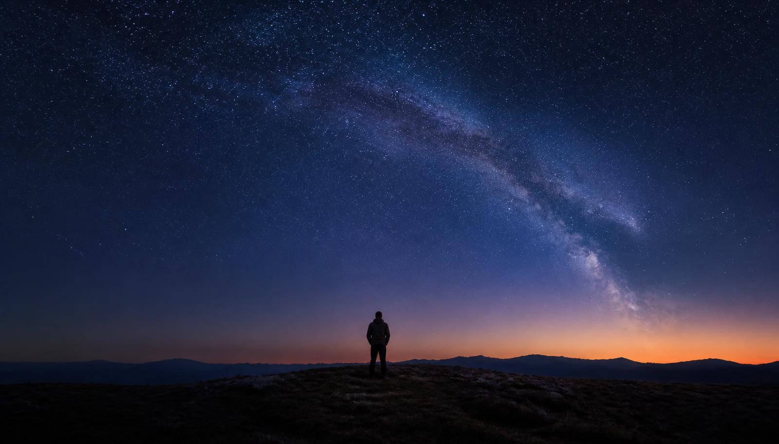 A single stargazer on a dark ridge under the Milky Way, with no telescope or equipment