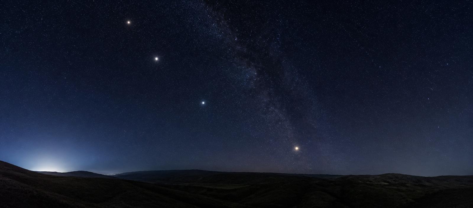 A chain of bright planets strung along an invisible diagonal line above a dark landscape